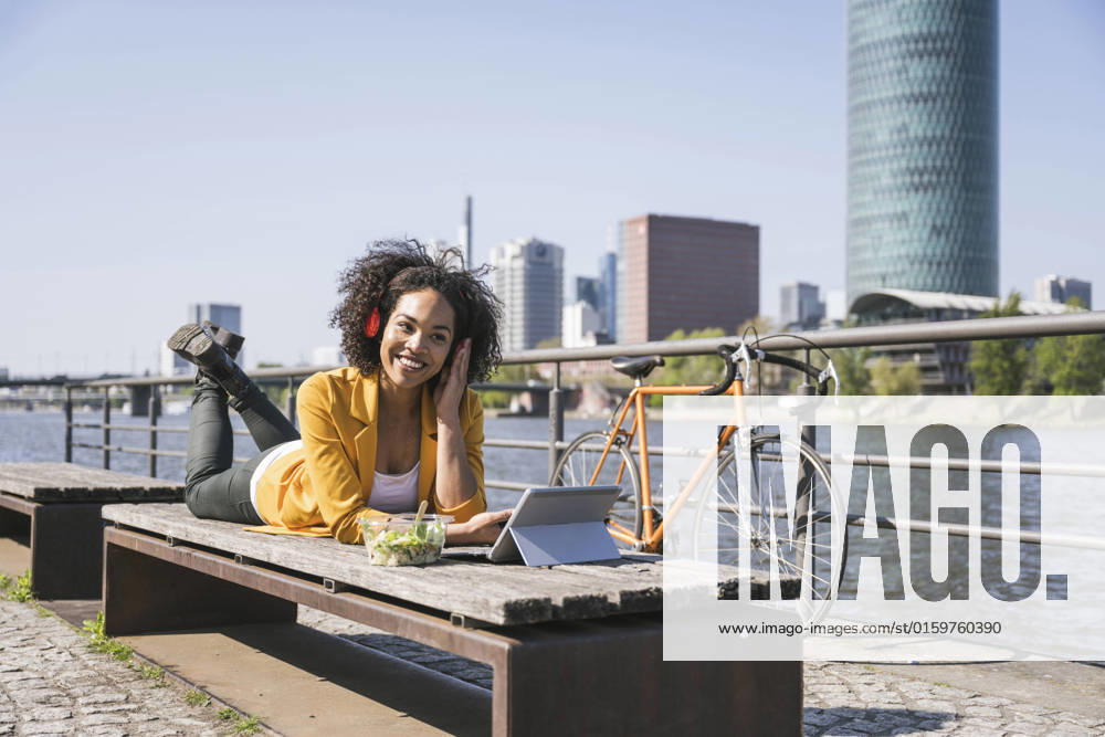 IMAGO Creative: Business - Work-Life Balance Smiling businesswoman listening music and using laptop on sunny day model released, Symbolfoto, UUF25929