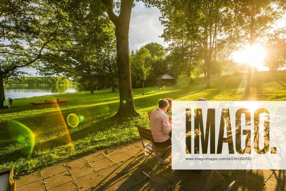 People sitting in the evening sun at a table of a garden restaurant and eating, Bavaria, Germany garden restaurant at a lakea small lake