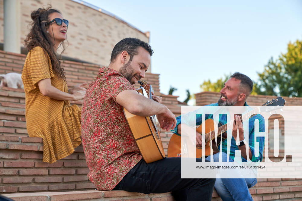 IMAGO Creative, Jahreszeit Sommer, Sommer in der Stadt From below content male musicians playing songs on acoustic guitars while sitting on steps with dog and woman on street, Model released JavierBermudez_RubenGuitarrist_36.jpg