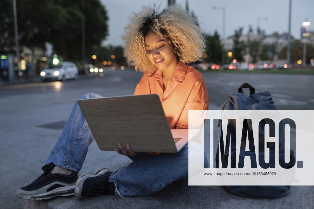 IMAGO Creative: Business, Innovative Technologie-Lösungen Woman using laptop sitting by backpack on sidewalk model released, Symbolfoto, JCCMF06660