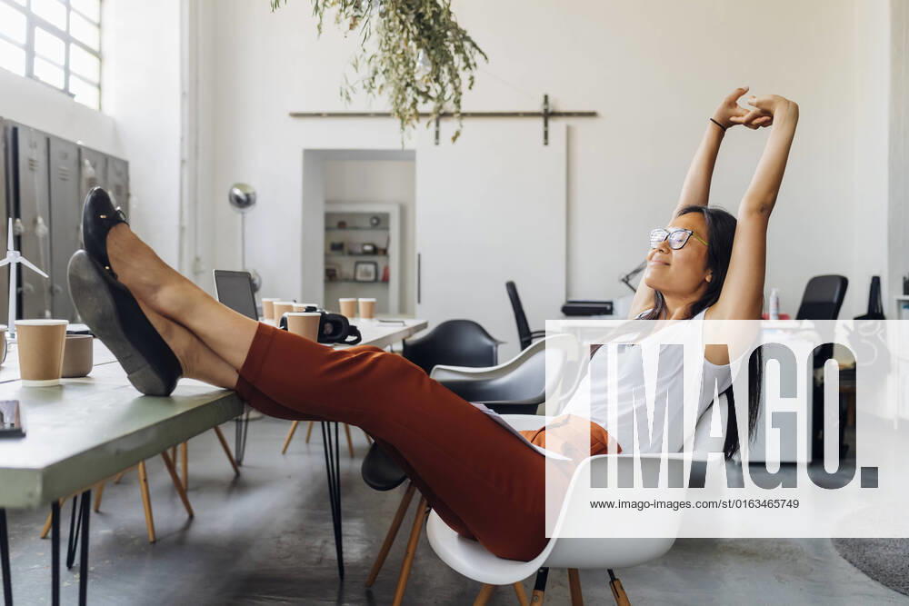 Smiling businesswoman stretching arms on chair at workplace model released, Symbolfoto property released, MEUF06737
