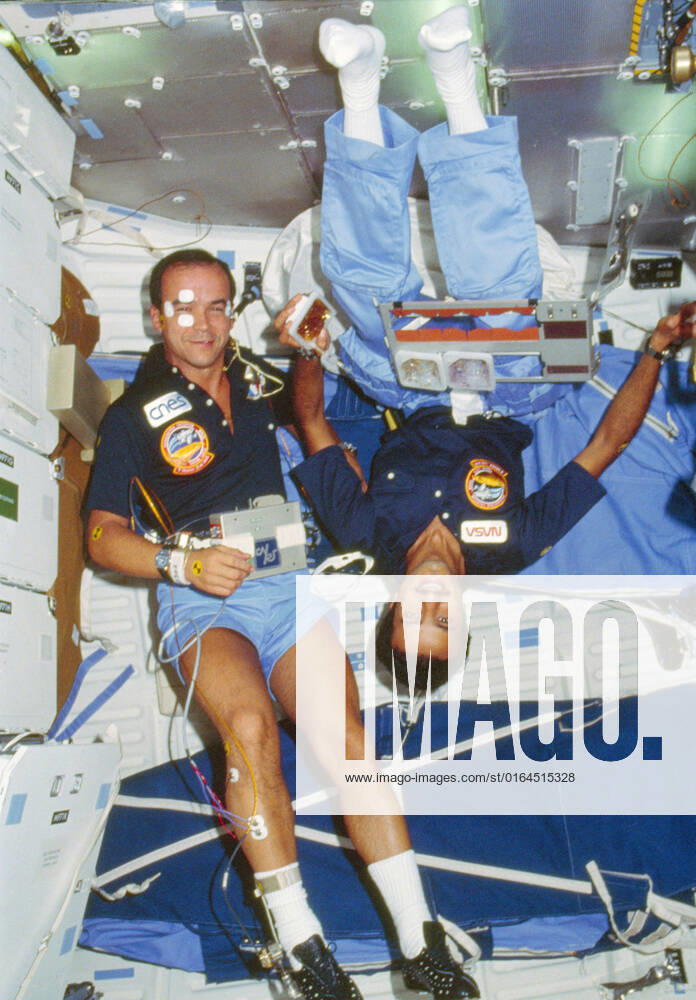 51G-102-035 (17-24 June 1985) --- The two payload specialists for the week-long flight share a middeck scene on the earth-orbiting Discovery. Sultan Salman Abdelazize Al-Saud (left) is in the midst of a meal while Patrick Baudry conducts a phase of the French Postural Experiment (FPE) on himself. Sleep restraints are in the background.