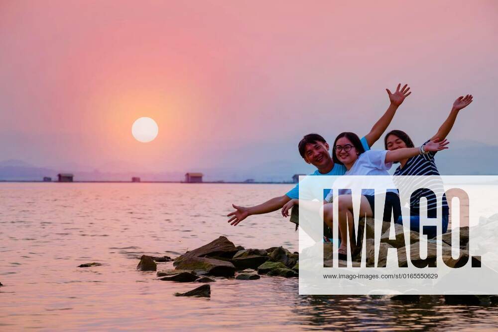 Asian family happy sitting on the waterfront, Asian family father mother and teenage daughter happy sitting on the waterfront at lake water sun in the orange sky beautiful nature landscape at sunset background, Krasiao Dam, Suphan Buri, Thailand model released, Symbolfoto , 31.12.2020,