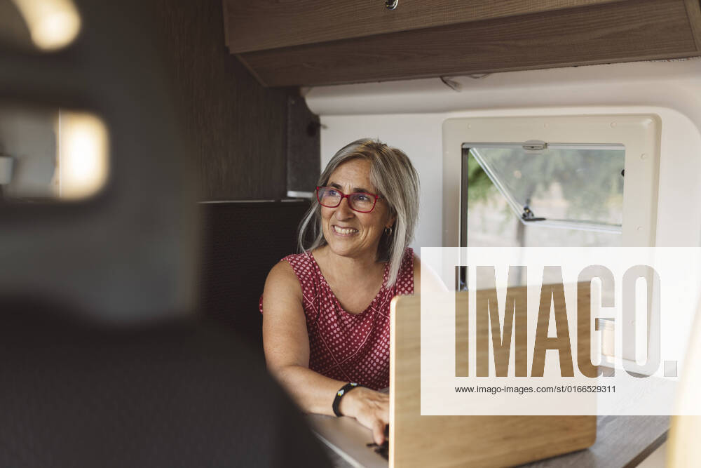 Smiling mature woman using laptop sitting in camper trailer model released, Symbolfoto, JCCMF06995