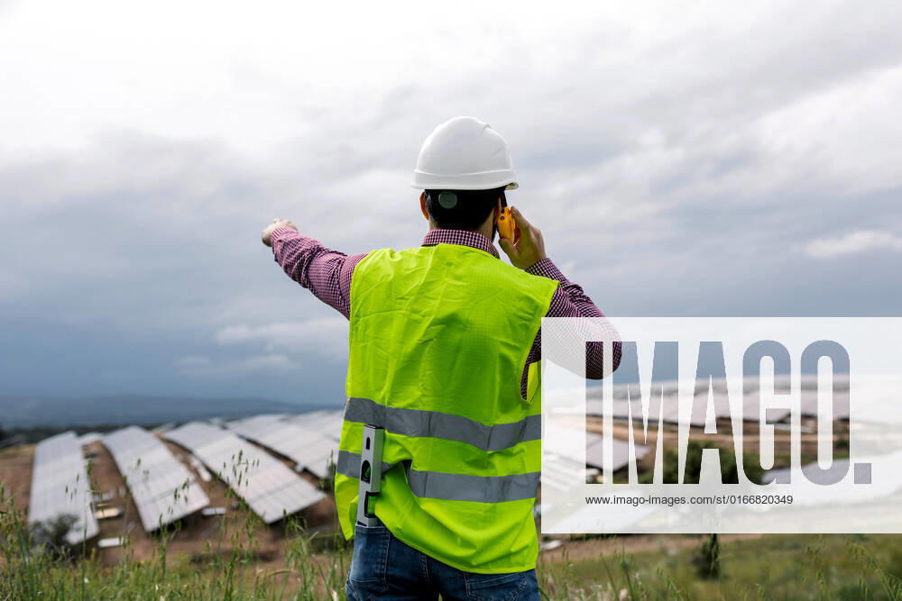 IMAGO Creative: Business, Innovative Technologie-L?sungen Back view of unrecognizable male speaking on walkie talkie against solar power station and overcast gray sky, Model released SergioVictorVega_SolarPanelArchitects_26