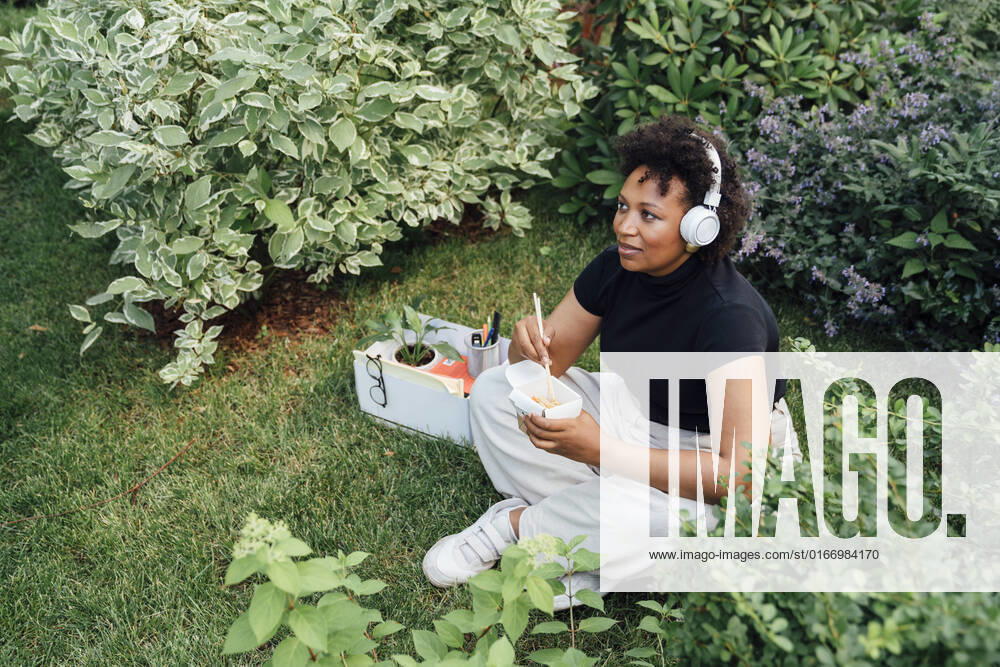 Businesswoman with take out food box listening music through wireless headphones sitting in park model released, Symbolfoto, VPIF06980