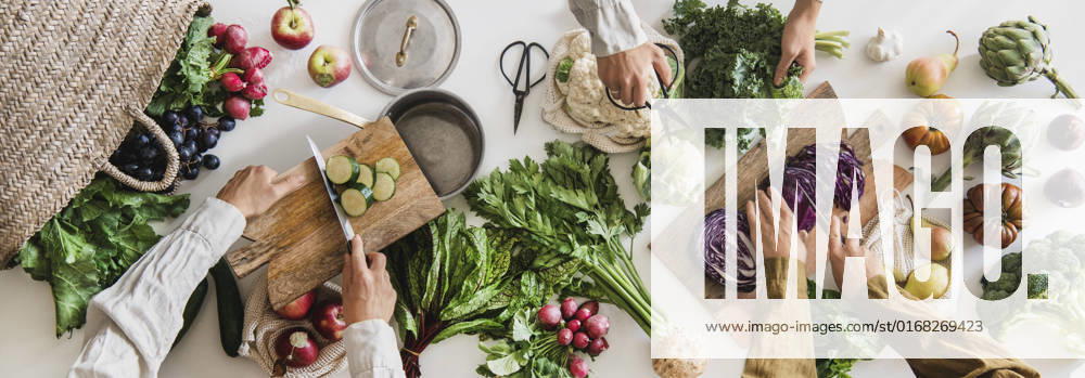 Fall vegetable vegetarian cooking background with greens and fruits Fall vegetarian cooking background. Female hands cutting greens and vegetable over table with fresh seasonal vegetables, greens, fruit from local grocery market, top view. Vegan, healthy, organic food