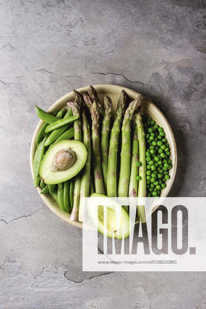 Young Green asparagus Variety of raw uncooked organic young green vegetables asparagus, peas, pod pea, avocado in ceramic plate over grey texture table background. Top view, space. Healthy eating