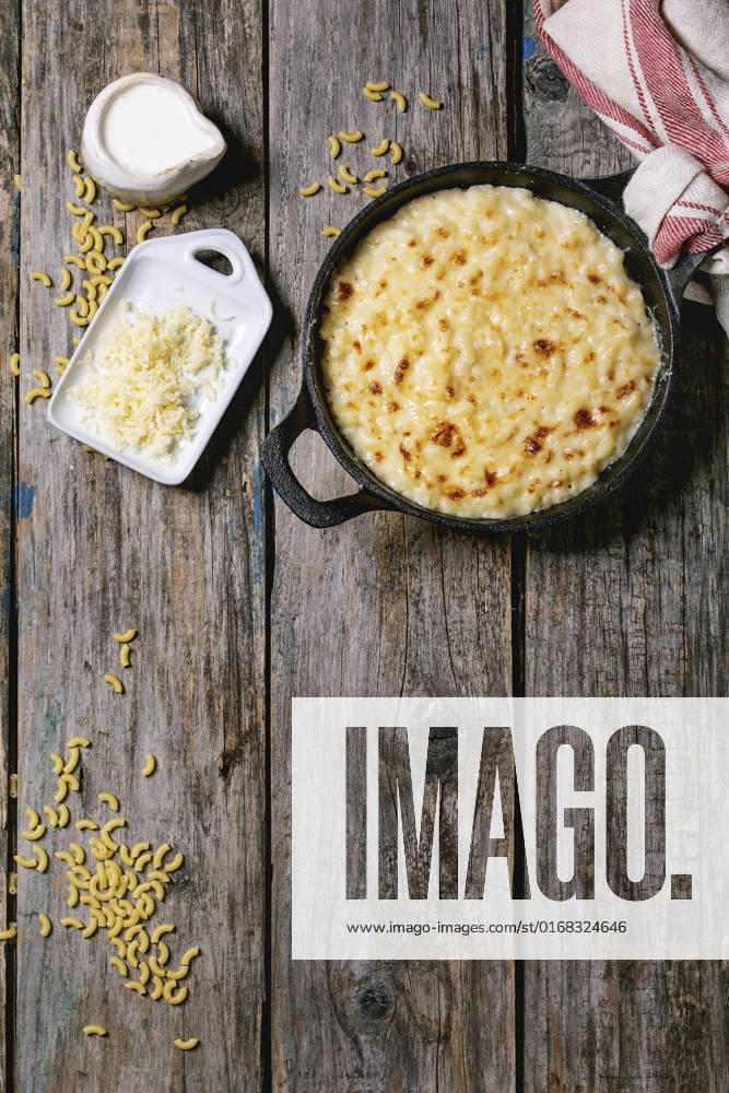 American dish mac and cheese Classic american dish baked mac and cheese in cast iron pan with kitchen towel and ingredients above over old wooden background. Flat lay, space