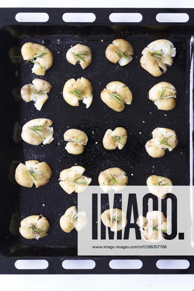 Smashed potatoes with black pepper and rosemary in a baking sheet.