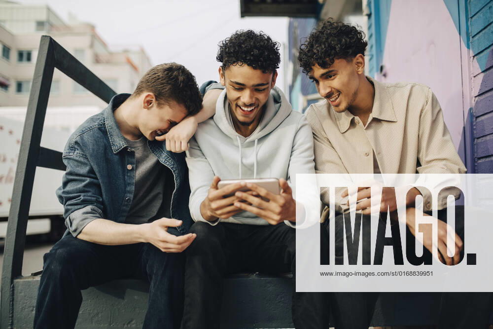 Happy man using smart phone while sitting with friends outdoors Sweden, Stockholm, model released