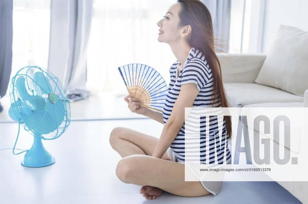 Young woman relax on floot in living room wave with hand fan and enjoying air flow from fan . Summer heat concept, Young woman relax on floot in living room wave with hand fan and enjoying air flow from fan . Summer heat concept, Young woman relax on floot in living room wave with hand fan and enjoying air flow from fan . Summer heat concept model released, Symbolfoto , 18.06.2022,