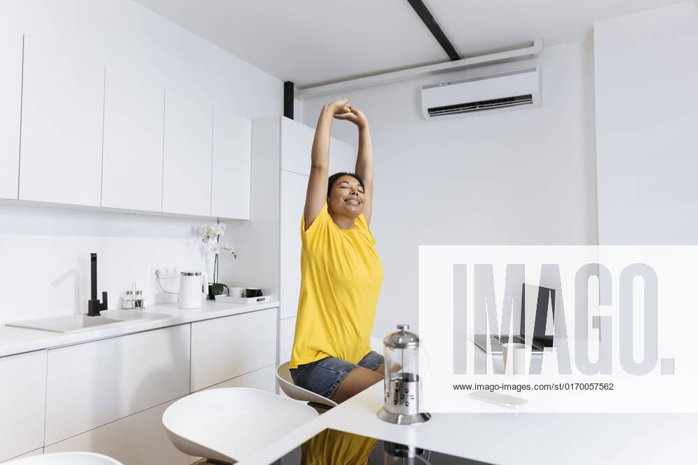 IMAGO Creative: Business, Innovative Technologie-Lösungen Happy woman stretching in kitchen taking a break fron freelance work model released, Symbolfoto property released, SIF00480