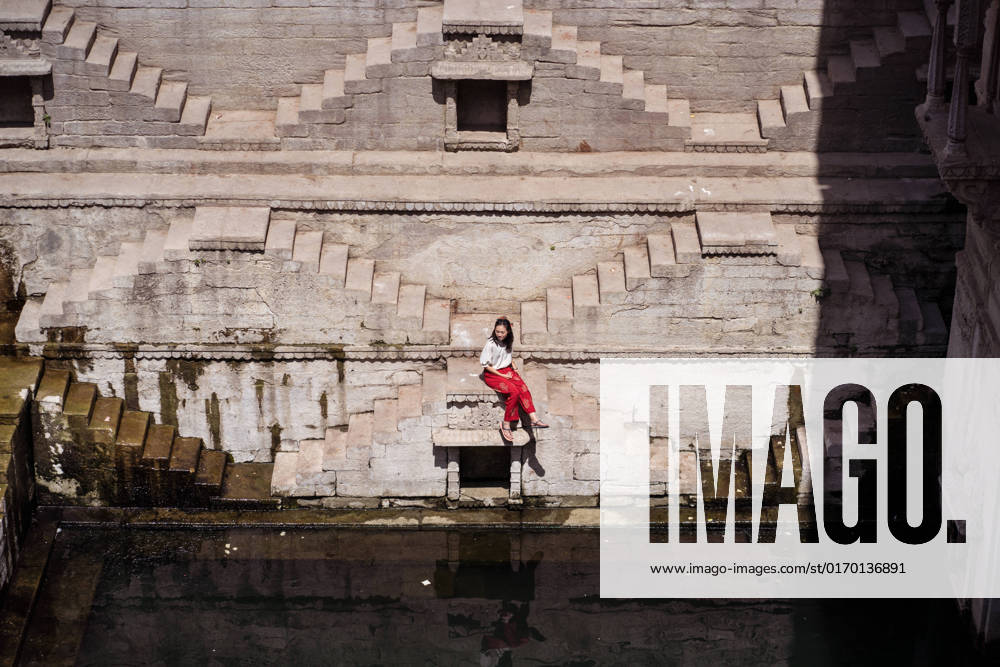 IMAGO Creative, Jahreszeit Sommer, Sommer in der Stadt From above young ethnic female tourist sitting on steps of Toorji well with water during sightseeing in India, Model released JuanAlbertoRuiz_ChiaInIndiaPart2_21