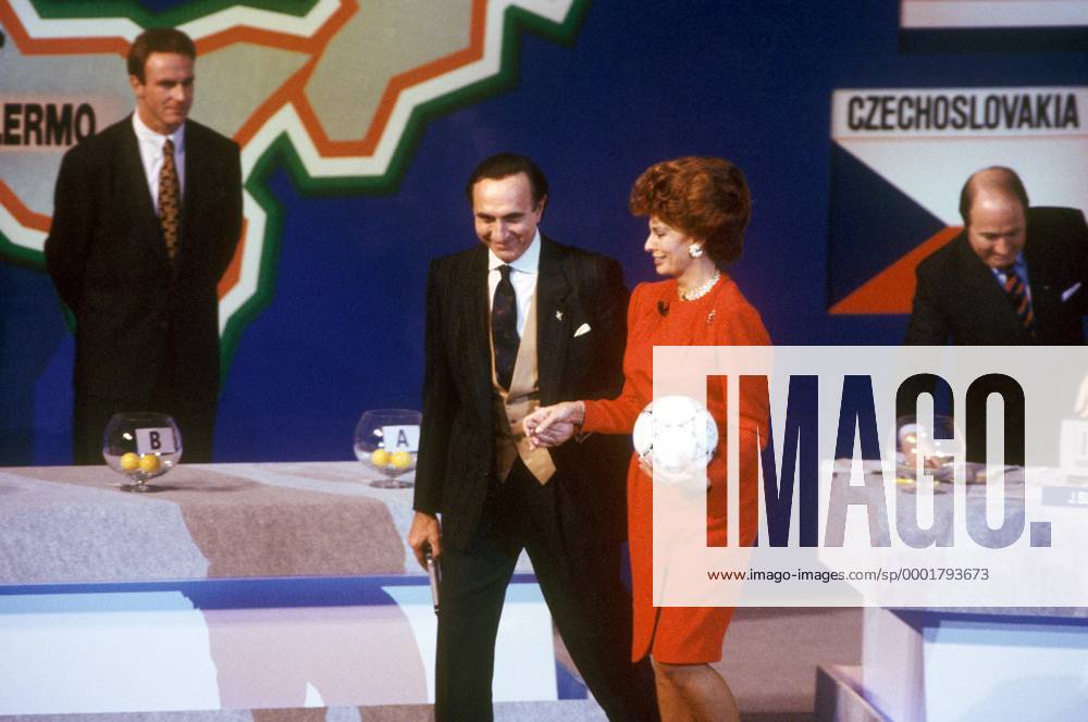 Auslosung zur WM 1990: die Schauspielerin Sophia Loren (Italien) schreitet elegant an der Hand des Moderators über die Bühne, im Hintergrund stehen Karl Heinz Rummenigge (li., BRD) und FIFA Generalsekretär Sepp Blatter (Schweiz) vor den Lostöpfen Fußball WM Herren Vorschau 1989 Weltmeisterschaft 1990, Gruppenauslosung, Vdia Gruppe Rom