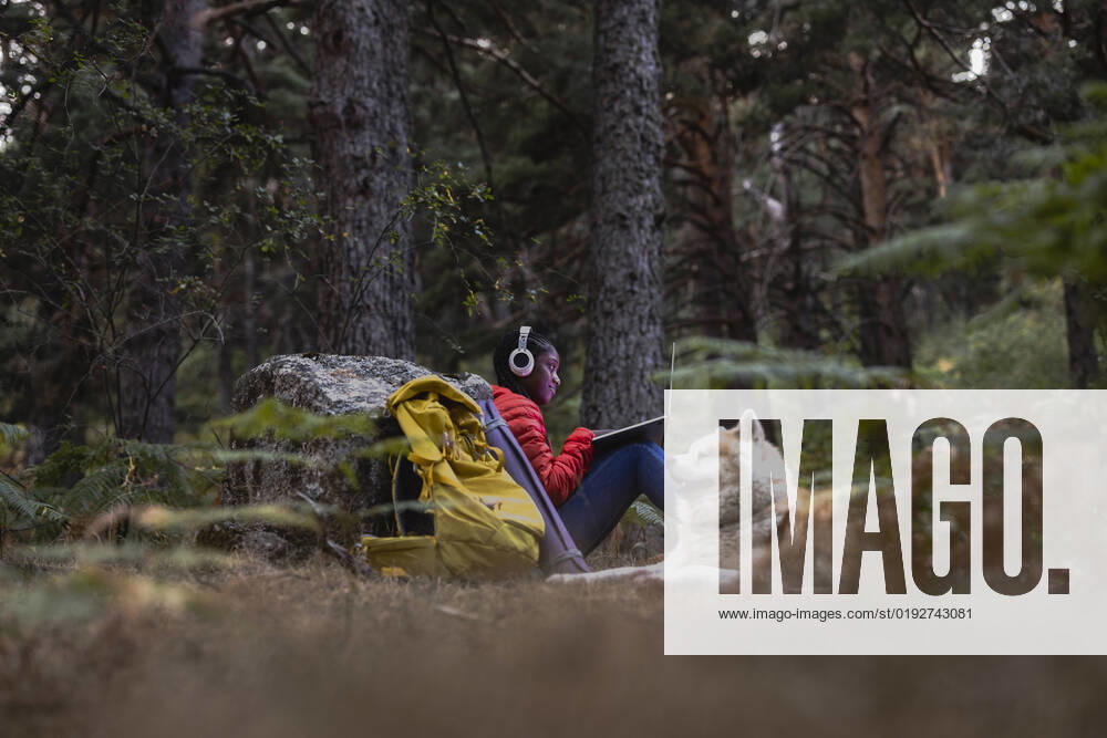 IMAGO Creative: Business - Work-Life Balance Woman wearing wireless headphones using laptop in forest model released, Symbolfoto property released, JCCMF07450