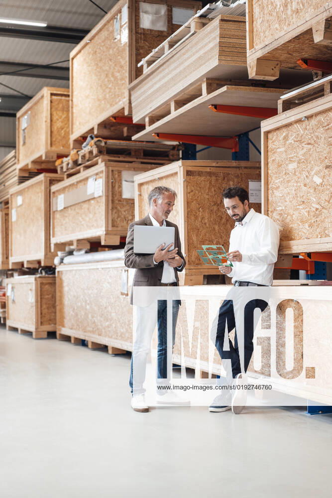 IMAGO Creative: Business, Inflation und Lieferketten Businessman holding laptop talking to colleague standing in warehouse model released, Symbolfoto property released, JOSEF13838
