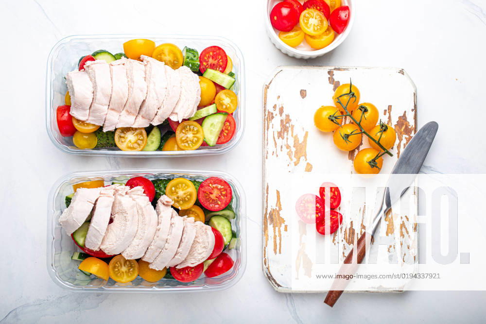 Meal prep lunch boxes containers with chicken and salad top view Healthy meal prep for lunch, diet boiled chicken fillet with vegetables salad in lunch boxes containers top view on white marble kitchen table background with knife and cutting board
