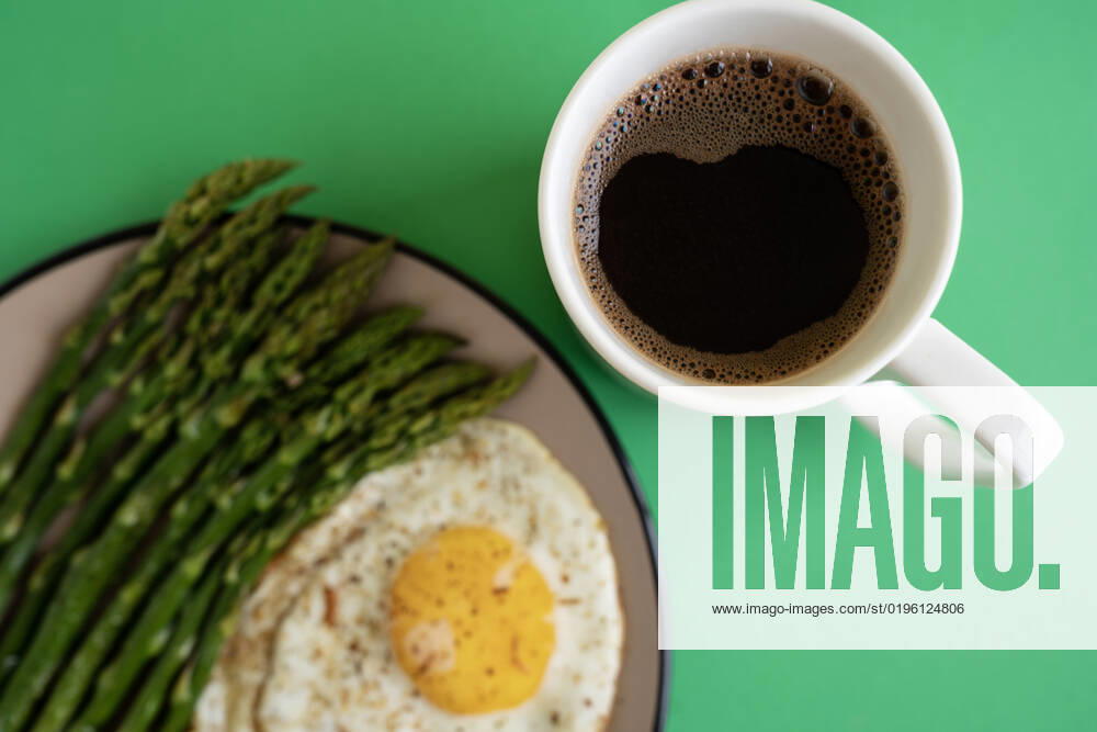 From above breakfast dish of fried egg with green asparagus server on plate next to cup of coffee on yellow background MaryMiro_ID3343_109454_002