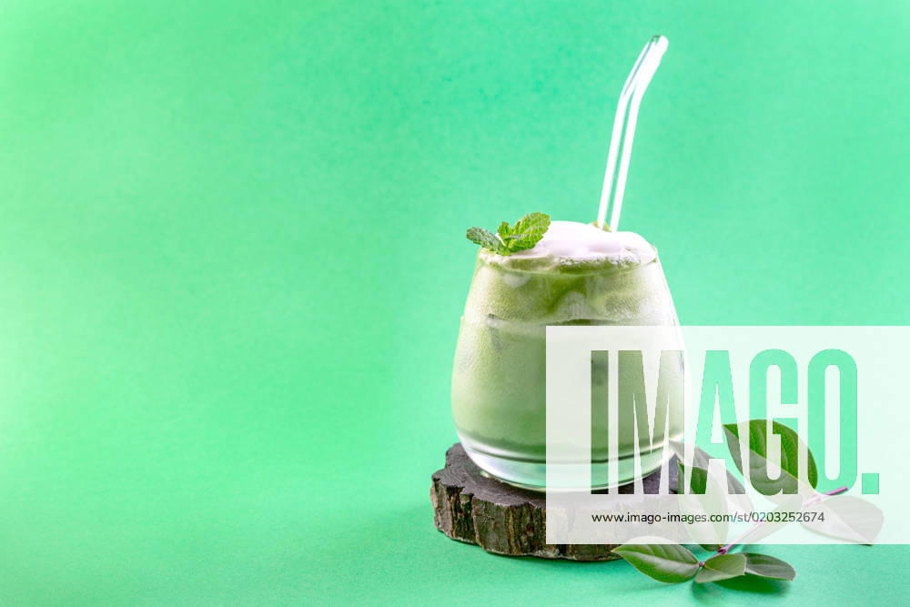 Ice green matcha latte. Glass of cold green matcha tea mixed with ice cubes and milk on a wooden stand. Copy space. Concept of iced summer drinks.
