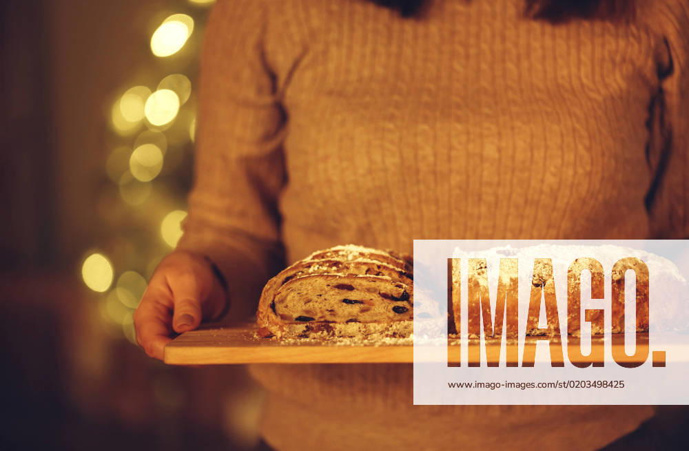 Cropped shot of woman holding delicious freshly baked homemade Christmas pie while standing against blurred xmas tree in background Cropped shot of woman holding delicious freshly baked homemade Christmas pie while standing against blurred xmas tree in background, preparing food for New Years Eve, selective focus on cake in hands. Stollen