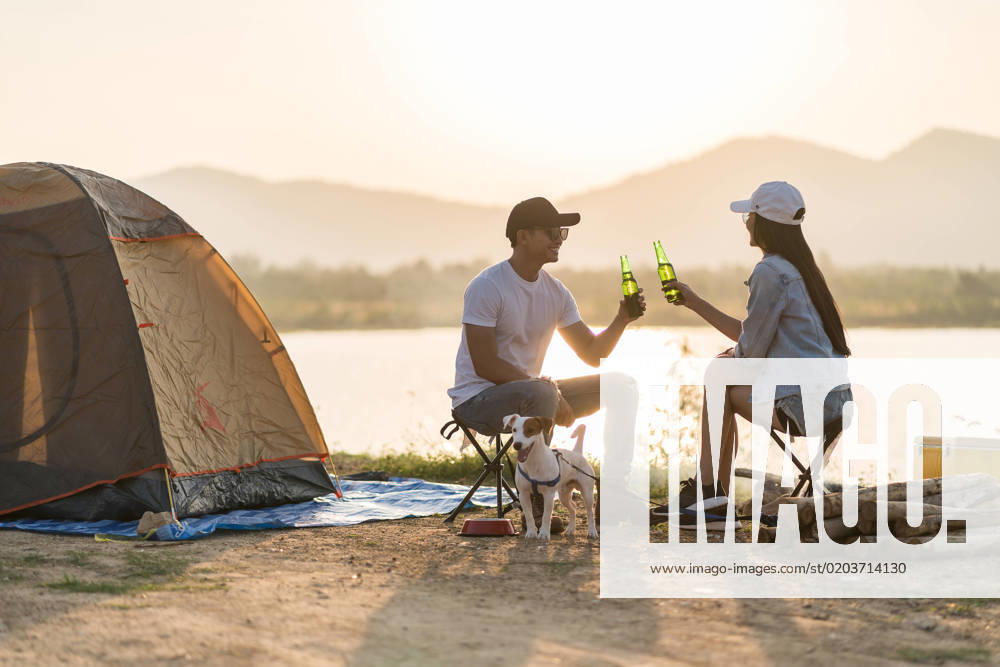 Young adult Asian couple drinking beer beside their tent with dog Young adult Asian couple drinking beer beside their tent campsite while sunset. Camping trip with dog outdoor activity campsite concept.