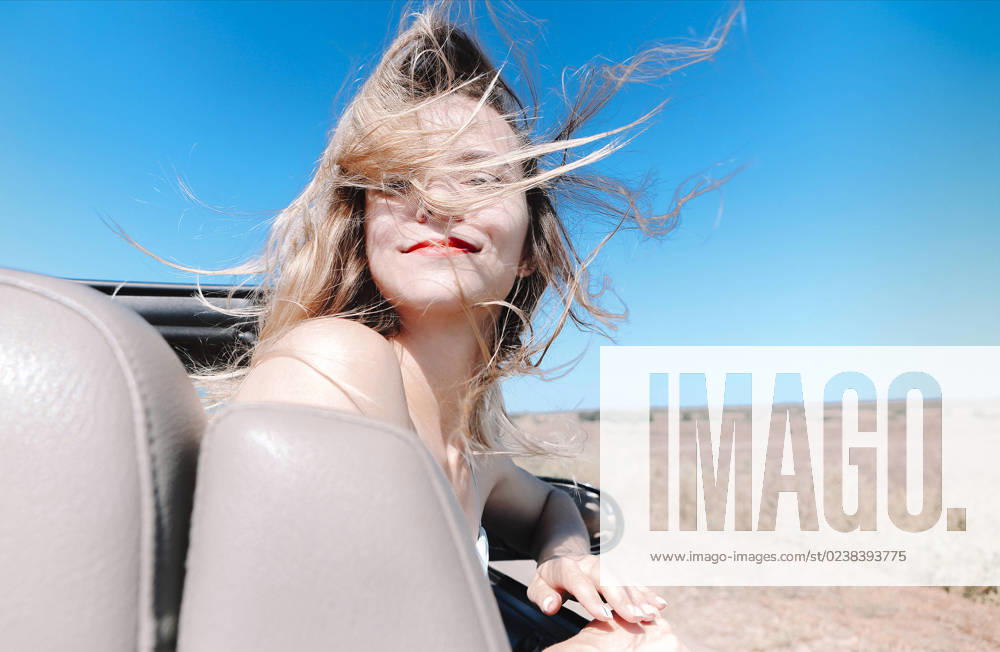 Happy woman sitting on passenger seat in car Joyful young female in summer clothes sitting on passenger seat of cabriolet and looking at camera over shoulder during road trip