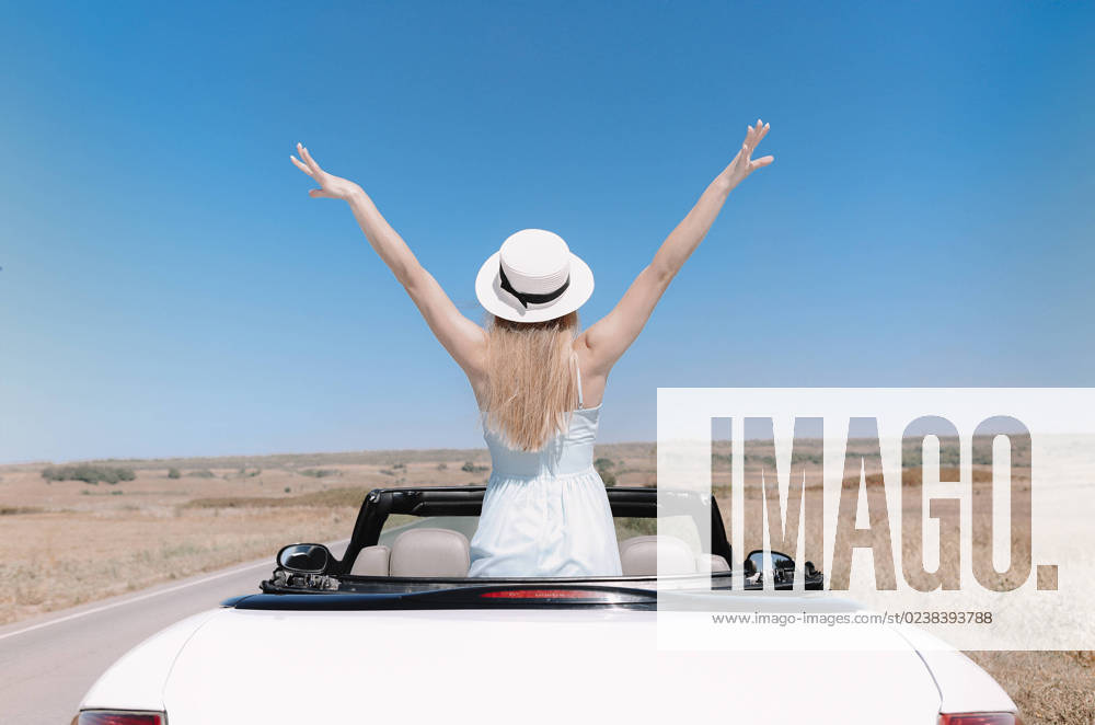 Happy woman sitting on passenger seat in car Back view of joyful young female in summer clothes in cabriolet during road trip