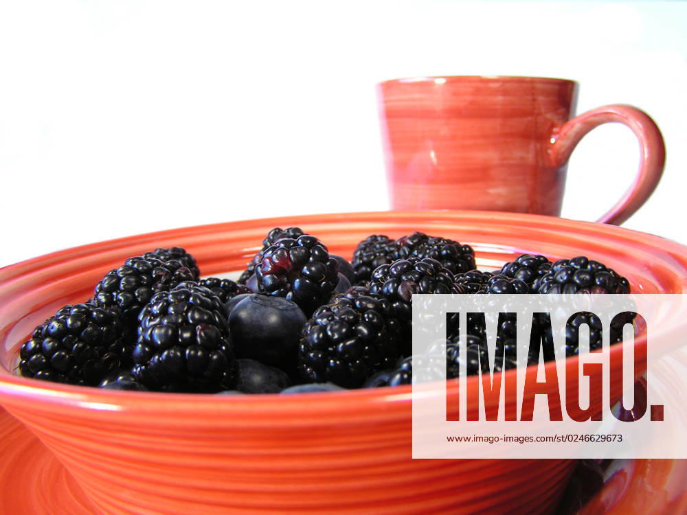 Mixed blueberries and blackberries in a bowl on a plate on a black placemat, with cup faded in background