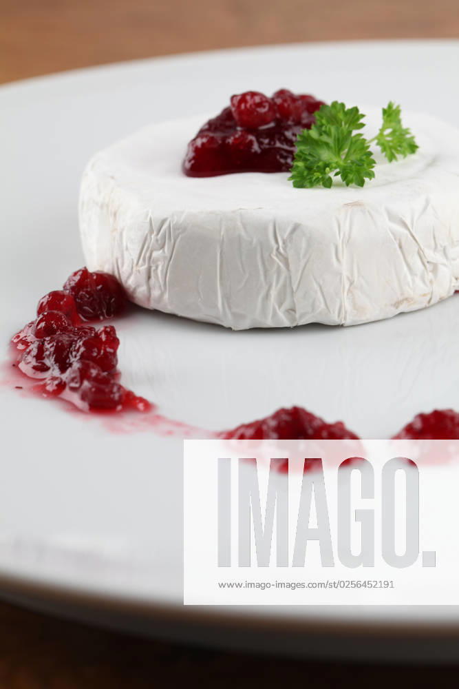 Camembert with cranberry jam and parsley on white plate. Shallow dof