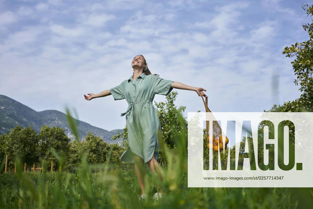 Smiling woman with arms outstretched standing in orange orchard model released, Symbolfoto property released, ANNF00183