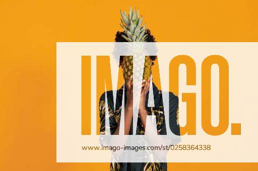 A Young African American woman with short hair dressed in a summer shirt posing with pineapple on an orange colored background *** einer Jung afrikanisch amerikanisch Frau mit Kurze Haare angezogen ÊIn einer Sommer Hemd posierend mit Ananas am An&Verkauf Orangefarbene farbige Hintergrund 8442344 ,model released, Symbolfoto RECORD DATE NOT STATED