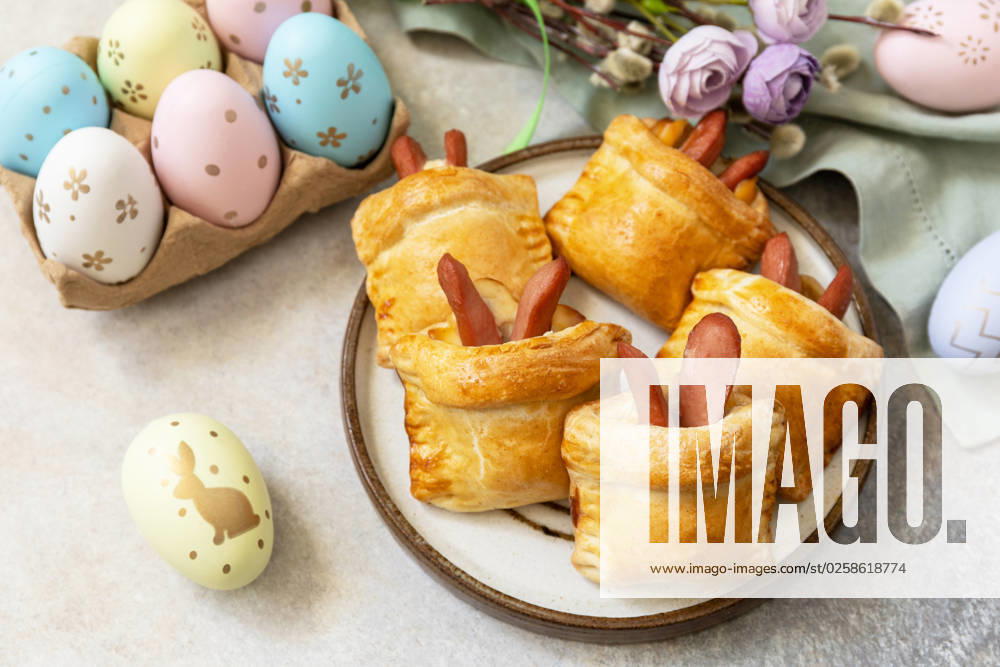 Buns in the form of an Easter rabbit from sausage and cheese in a yeast dough with colored eggs on a gray stone background. Traditional Easter symbols and food. Buns in the form of an Easter rabbit from sausage and cheese in a yeast dough with colored eggs on a gray stone background. Traditional Easter symbols and food.