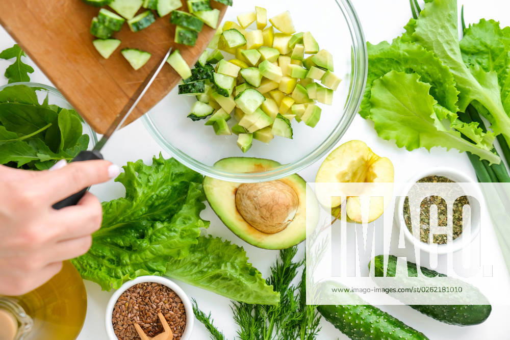 Woman cooking salad of fresh green vegetables and herbs. Raw food concept. Vegan menu. Cooking healthy diet or vegetarian food. Female hands cut cucumber on cutting board surrounded by green vegetables. Step by step recipe. Woman cooking salad of fresh green vegetables and herbs. Cooking healthy diet or vegetarian food. Female hands cut cucumber on cutting board surrounded by green vegetables. Step by step recipe. Healthy eating. Ingredients for salad. Pattern flat lay with healthy vegetarian meal ingredients. Raw food concept. A variety of organic fruits and vegetables with avocado. Vegan menu. Fresh spinach and green onion leaves.