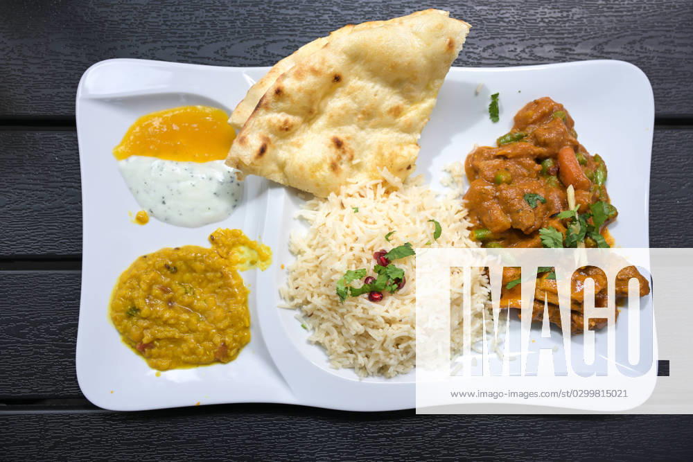 IMAGO Creative, Food, Brot, Naan Indian meat dish of beef with sauce, rice, bread, lentils and dips, served on a white plate and a dark table, high angle view from above, selected focus Indian meat dish of beef with sauce, rice, bread, lentils and dips, served on a white plate and a dark table, high angle view from above, selected focus