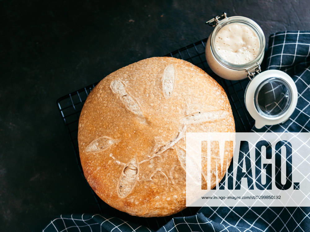 Wheat round sourdough bread, copy space, top view Wheat round sourdough bread and sourdoug starter in glass jar. Top view of delicious homemade sourdough bread on black background with copy space. Home made sourdough bread making concept.