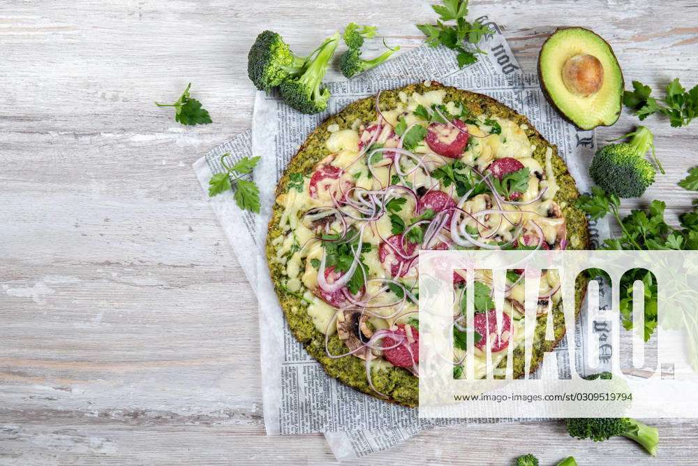 Crust Broccoli base low carbs keto pizza with salami, avocado on vintage newspapper. Top view Crust Broccoli base low carbs keto pizza with salami, avocado on vintage newspapper. Top view.