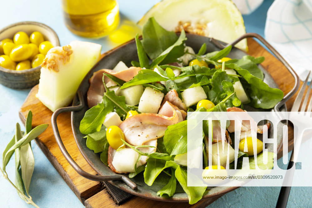 Traditional Spanish and Italian appetizer. Summer mediterranean salad with melon, bacon, olives, white cheese and arugula on blue stone background. Traditional Spanish and Italian appetizer. Summer mediterranean salad with melon, bacon, olives, white cheese and arugula on blue stone background.