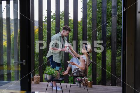 A young couple clinking with wine outdoors, weekend away in tiny house in countryside, sustainable living. love, wine, couple, woman, man, outdoor, happy, terrace, romance, romantic, together, young, drink, glass, person, smiling, caucasian, celebration, lifestyle, garden, party, relationship, two, alcohol, cheerful, vacation, tourism, closeness, date, honeymoon, newlyweds, lover, positive, togetherness, drinking, champagne, evening, holding, tiny house, holiday, nature, off beat, relax, meditation, digital detox, candle, hygge, travel, weekend away
