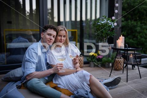 A young couple clinking with wine outdoors, weekend away in tiny house in countryside, sustainable living. love, wine, couple, woman, man, outdoor, happy, terrace, romance, romantic, together, young, drink, glass, person, smiling, caucasian, celebration, lifestyle, garden, party, relationship, two, alcohol, cheerful, vacation, tourism, closeness, date, honeymoon, newlyweds, lover, positive, togetherness, drinking, champagne, evening, holding, tiny house, holiday, nature, off beat, relax, meditation, digital detox, candle, hygge, travel, weekend away