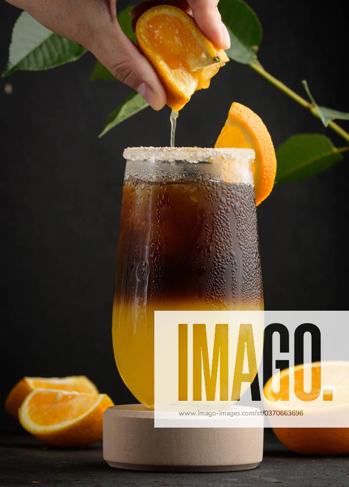 Iced coffee with orange juice in a transparent glass, a woman s hand squeezes an orange slice into a bubble drink Iced coffee with orange juice in a transparent glass, a woman s hand squeezes an orange slice into a bubble drink