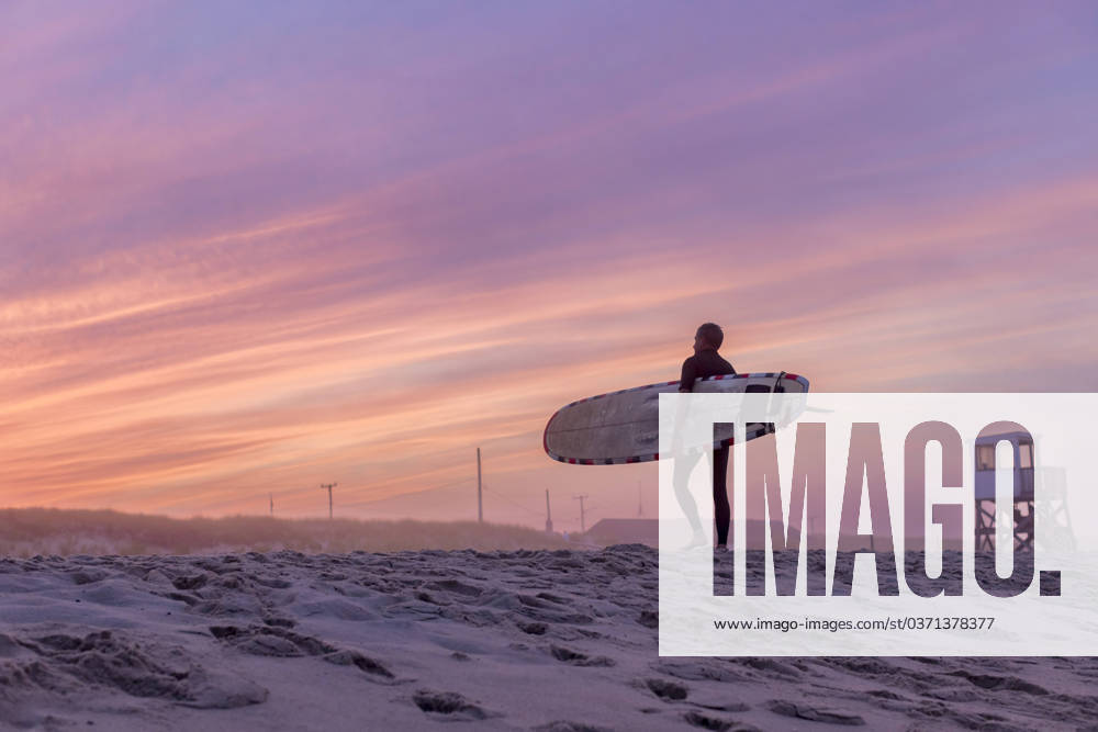 A surfer walks on the beach with his surfboard at sunset Orleans, Massachusetts, United States CR_JUCU231129F1-1272598-01 ,model released, Symbolfoto
