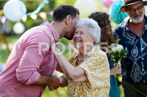 Garden birthday party for senior lady. Beautiful senior birthday woman receiving birthday wishes. birthday woman senior hugging gifts garden birthday party beautiful woman lady receiving gift wishes embrace smile friends family grandmother grandson celebration joy happiness presents outdoors event festivity gathering special occasion surprise smiles enjoyment togetherness love affection decorations cake memories balloons laughter congratulations entertainment bonding delight cheerful atmosphere friendship gratitude copy space gray hair pearls