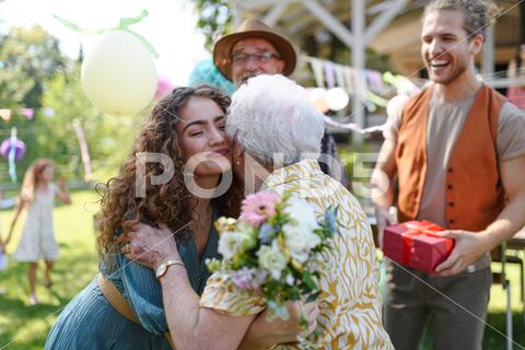 Garden birthday party for senior lady. Beautiful senior birthday woman hugging her granddaughter. birthday woman senior hugging gifts garden birthday party beautiful woman lady receiving gift granddaughter grandmother embrace smile friends family kiss on cheek celebration joy happiness presents outdoors event festivity gathering special occasion surprise smiles enjoyment togetherness love affection decorations cake memories balloons laughter congratulations wishes entertainment bonding delight cheerful atmosphere friendship gratitude copy space gray hair pearls