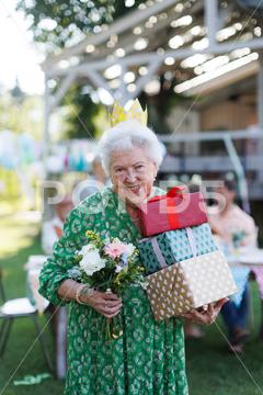Garden birthday party for senior lady. Beautiful senior birthday woman with paper crown on head and gifts in hands. birthday woman senior crown paper flowers gifts garden birthday party beautiful woman lady receiving gift smile friends family grandmother celebration joy happiness presents outdoors event festivity gathering special occasion surprise smiles enjoyment togetherness love affection decorations cake memories balloons laughter congratulations wishes entertainment bonding delight cheerful atmosphere friendship gratitude copy space gray hair pearls