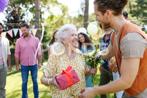 Garden birthday party for senior lady. Beautiful senior birthday woman receiving birthday wishes and gifts. birthday woman senior hugging gifts garden birthday party beautiful woman lady receiving gift wishes embrace smile friends family grandmother grandson celebration joy happiness presents outdoors event festivity gathering special occasion surprise smiles enjoyment togetherness love affection decorations cake memories balloons laughter congratulations entertainment bonding delight cheerful atmosphere friendship gratitude copy space gray hair pearls