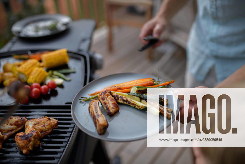 Father putting grilled meat and vegetable on plate to his son during family summer garden party. A father putting grilled meat and vegetable on plate to his son during family summer garden party. model released