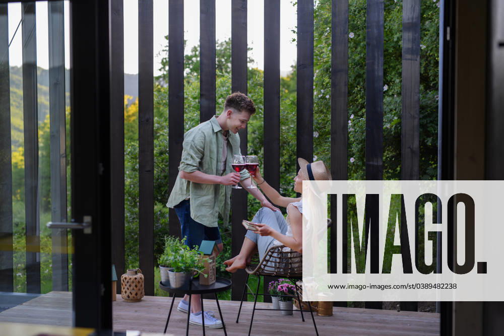 Young couple clinking with wine outdoors, weekend away in tiny house in countryside, sustainable living. A young couple clinking with wine outdoors, weekend away in tiny house in countryside, sustainable living. model released