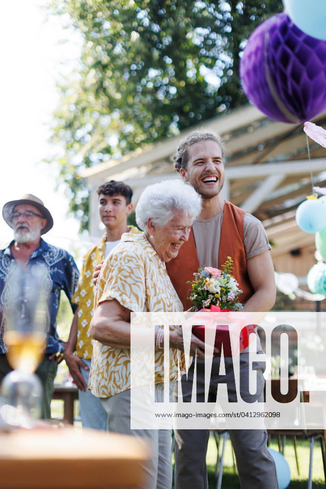 Garden birthday party for senior lady. Beautiful senior birthday woman receiving birthday gift from grandson. Garden birthday party for senior lady. Beautiful senior birthday woman receiving birthday wishes and gifts from grandson. model released