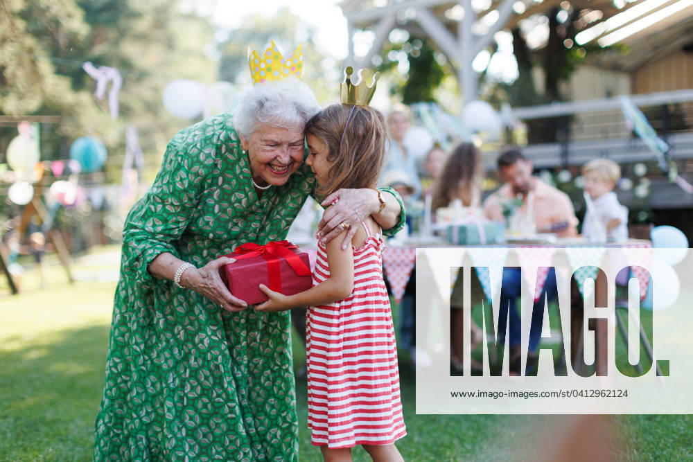Garden birthday party for senior lady. Beautiful senior birthday woman receiving gift from granddaughter. Garden birthday party for senior lady. Beautiful senior birthday woman receiving gift from granddaughter, hugging. model released